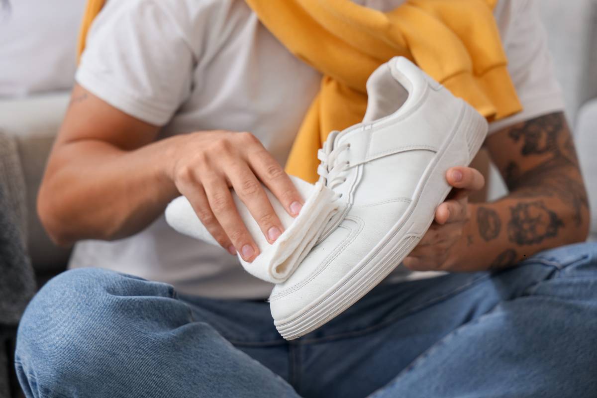 Person cleaning white sneakers at home using a brush and soapy water